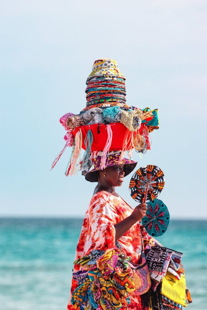 African woman in traditional attire with crafts at Sardinia beach.