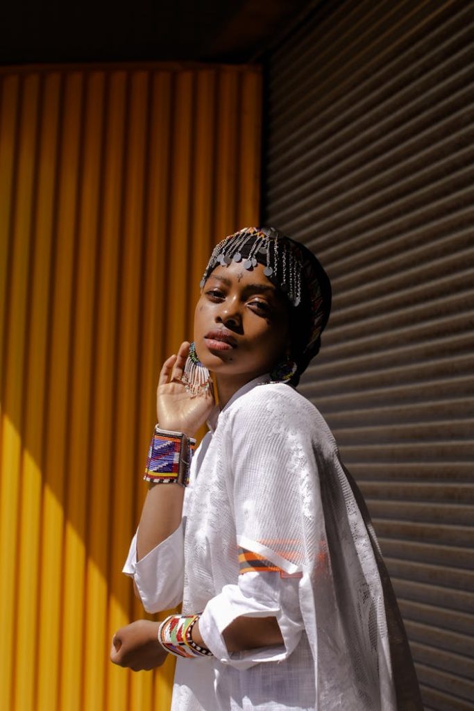 Elegant African woman poses fashionably in vibrant traditional attire against a colorful urban backdrop.